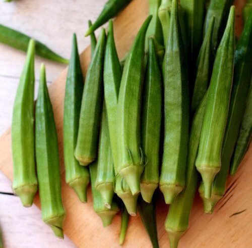 Fresh green okra pods arranged on a wooden board.