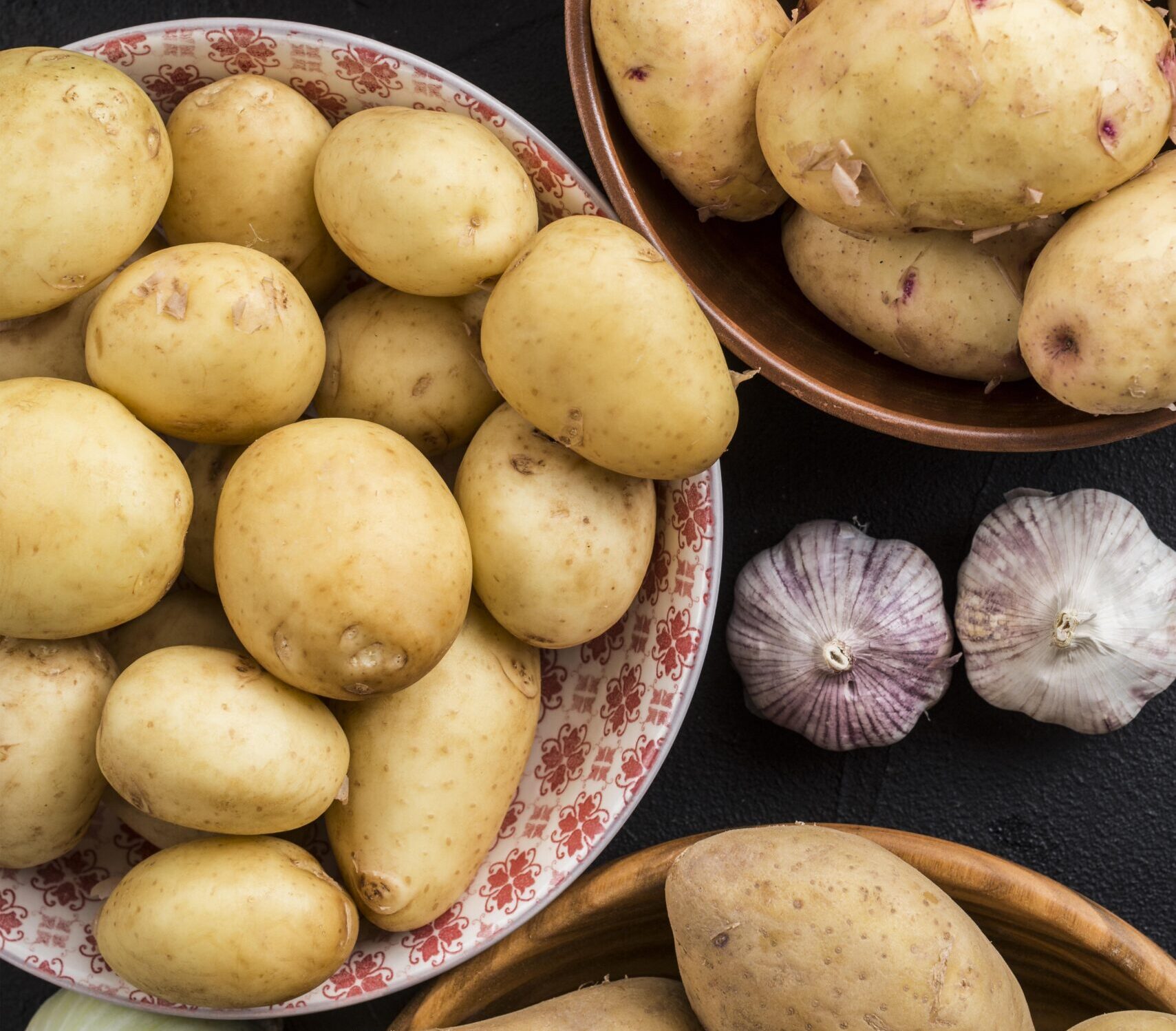 Fresh potatoes displayed in bowls with garlic and onions.