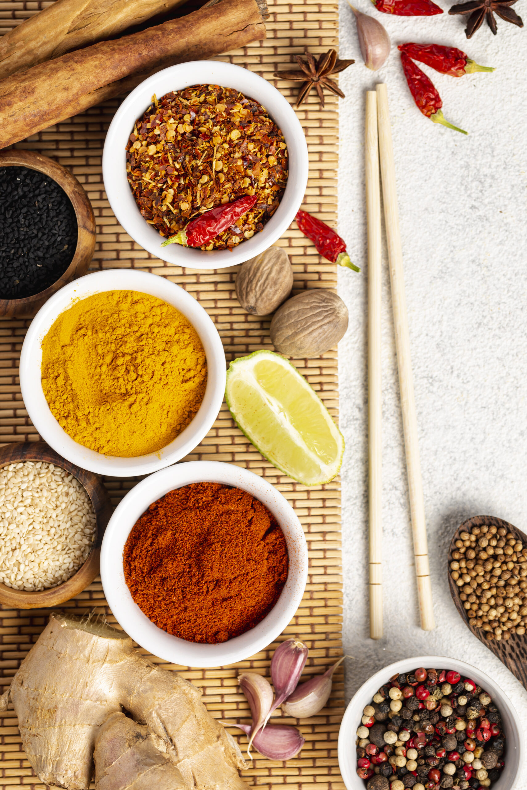 Assorted Indian spices including turmeric powder, red chilli powder, black pepper, coriander seeds, ginger, and garlic arranged on a bamboo mat.