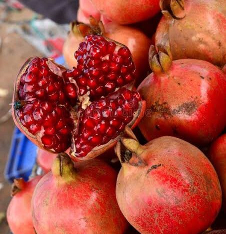Fresh Indian pomegranates with opened fruit showing juicy red seeds.